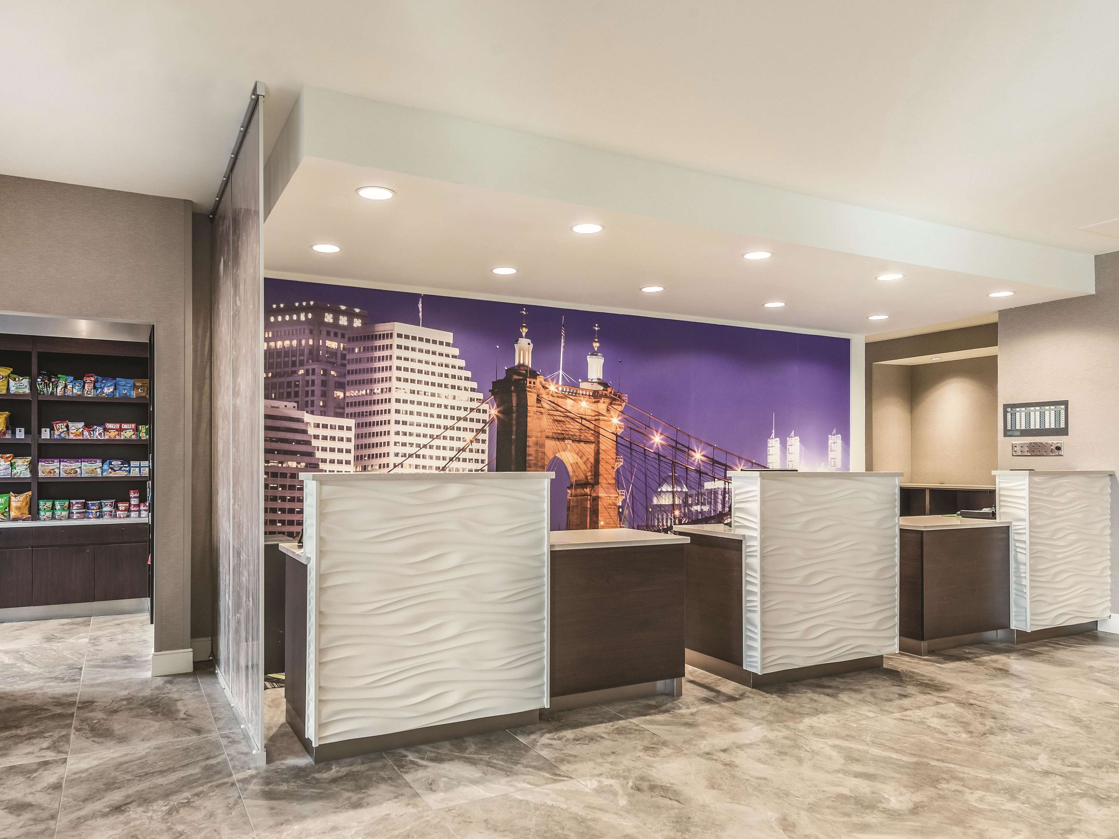 Zona de recepción de un hotel con un mural de paisaje urbano, una barra de aperitivos y un mostrador de recepción moderno.