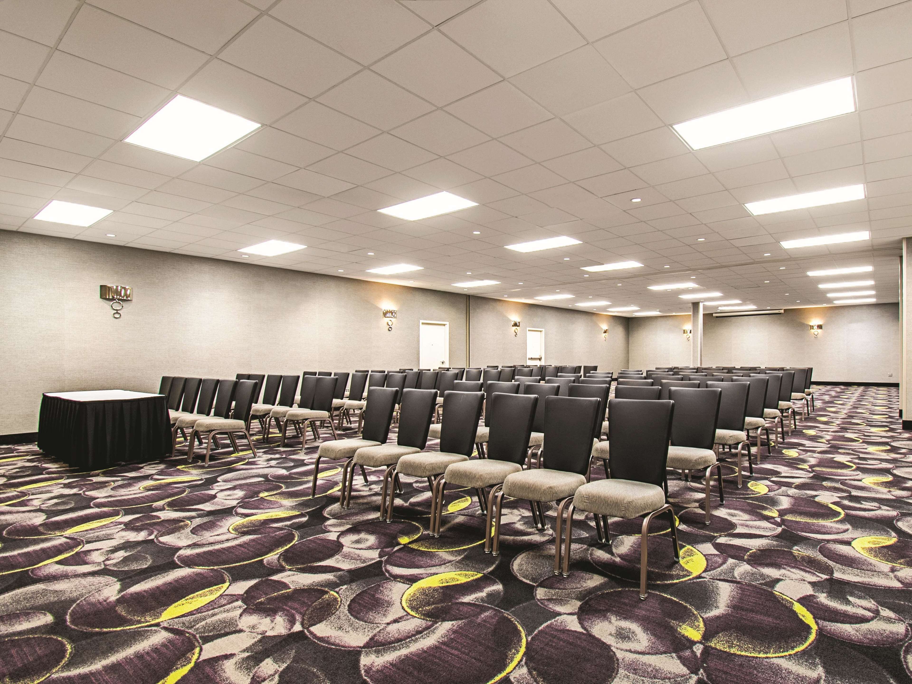 Une salle de conférence avec des rangées de chaises, une table et un sol recouvert de moquette.