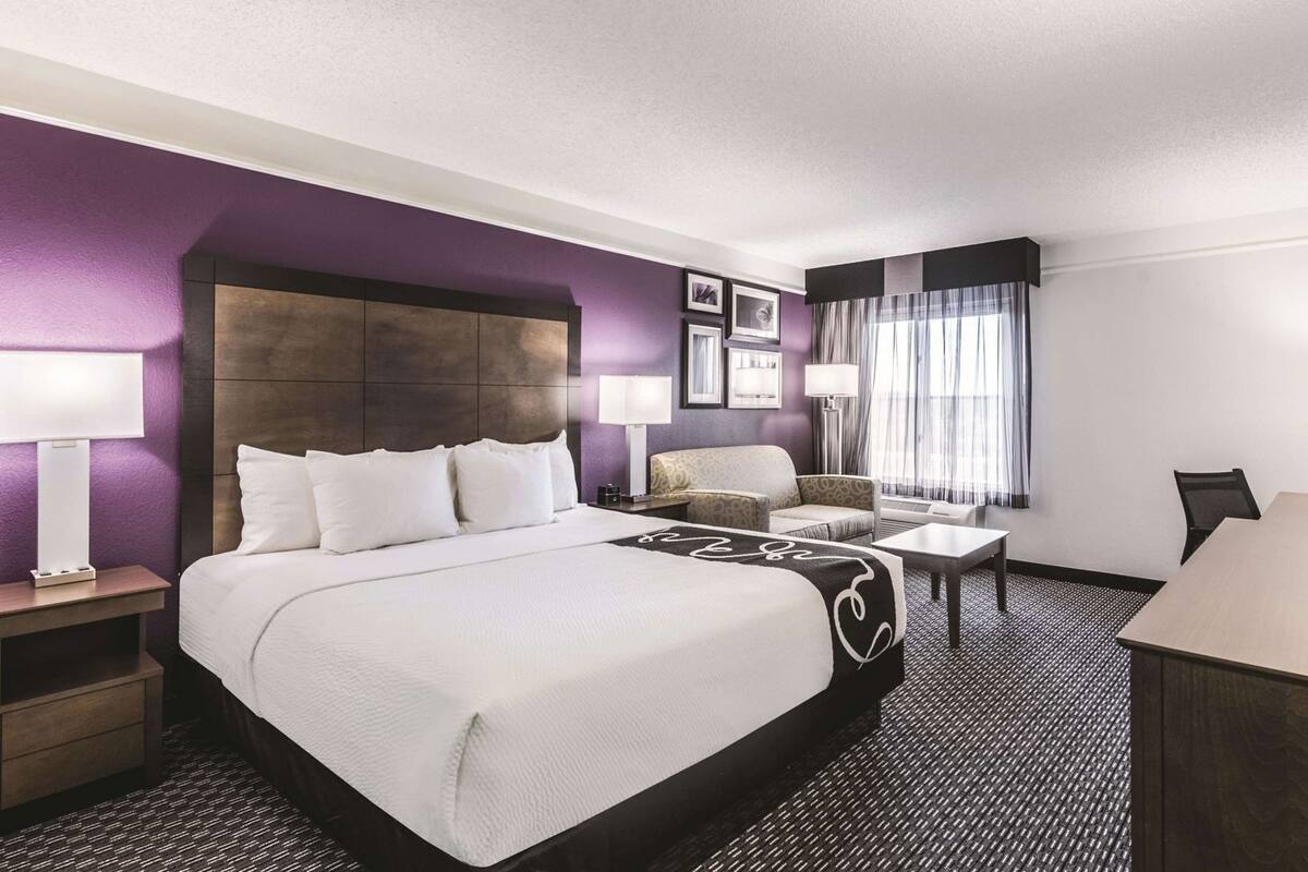 Una habitación de hotel con una cama grande, un escritorio, una silla y una ventana con cortinas.