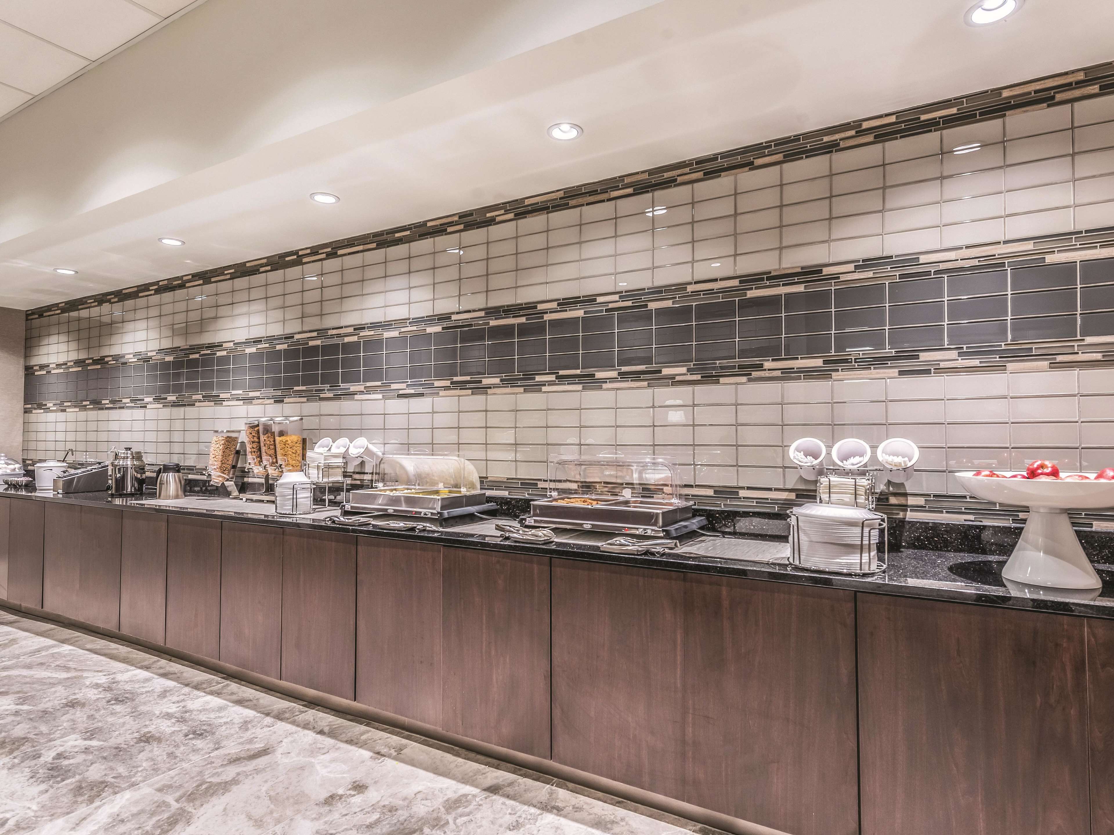 A modern hotel kitchen with a long counter, equipped with various appliances and food dispensers.