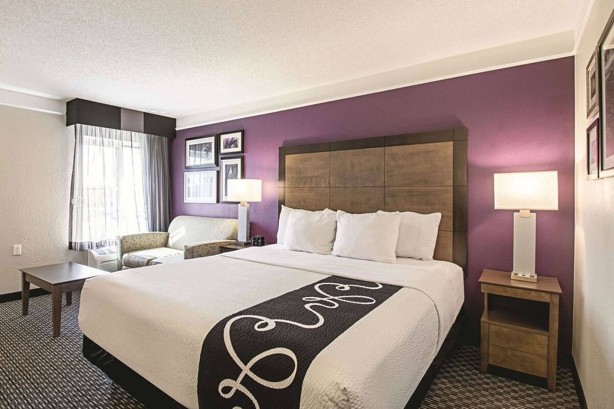 A hotel room with a large bed, two bedside tables, a chair, and a window with curtains.