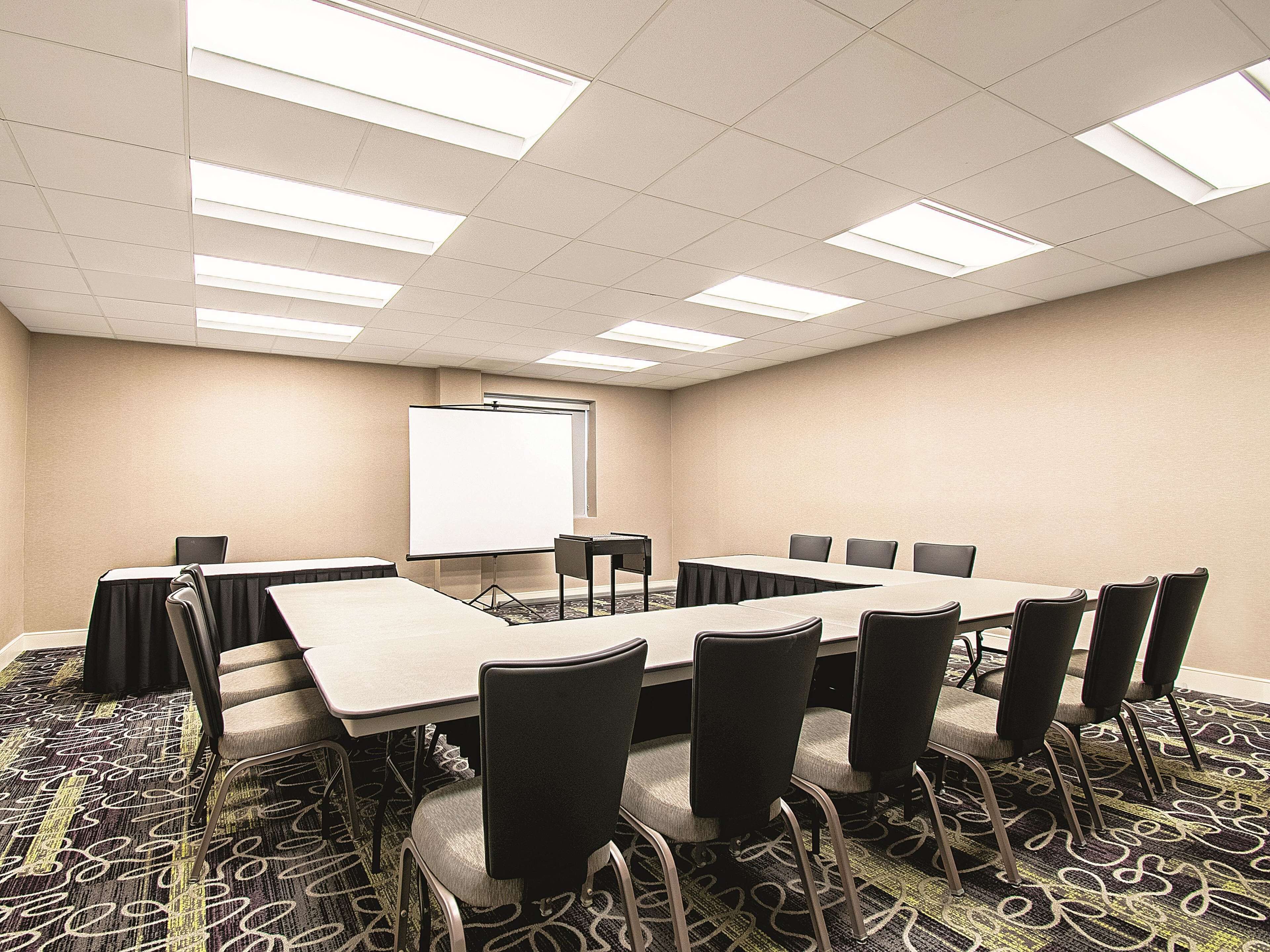 A conference room with a long table, chairs, a projector screen, and a carpeted floor.