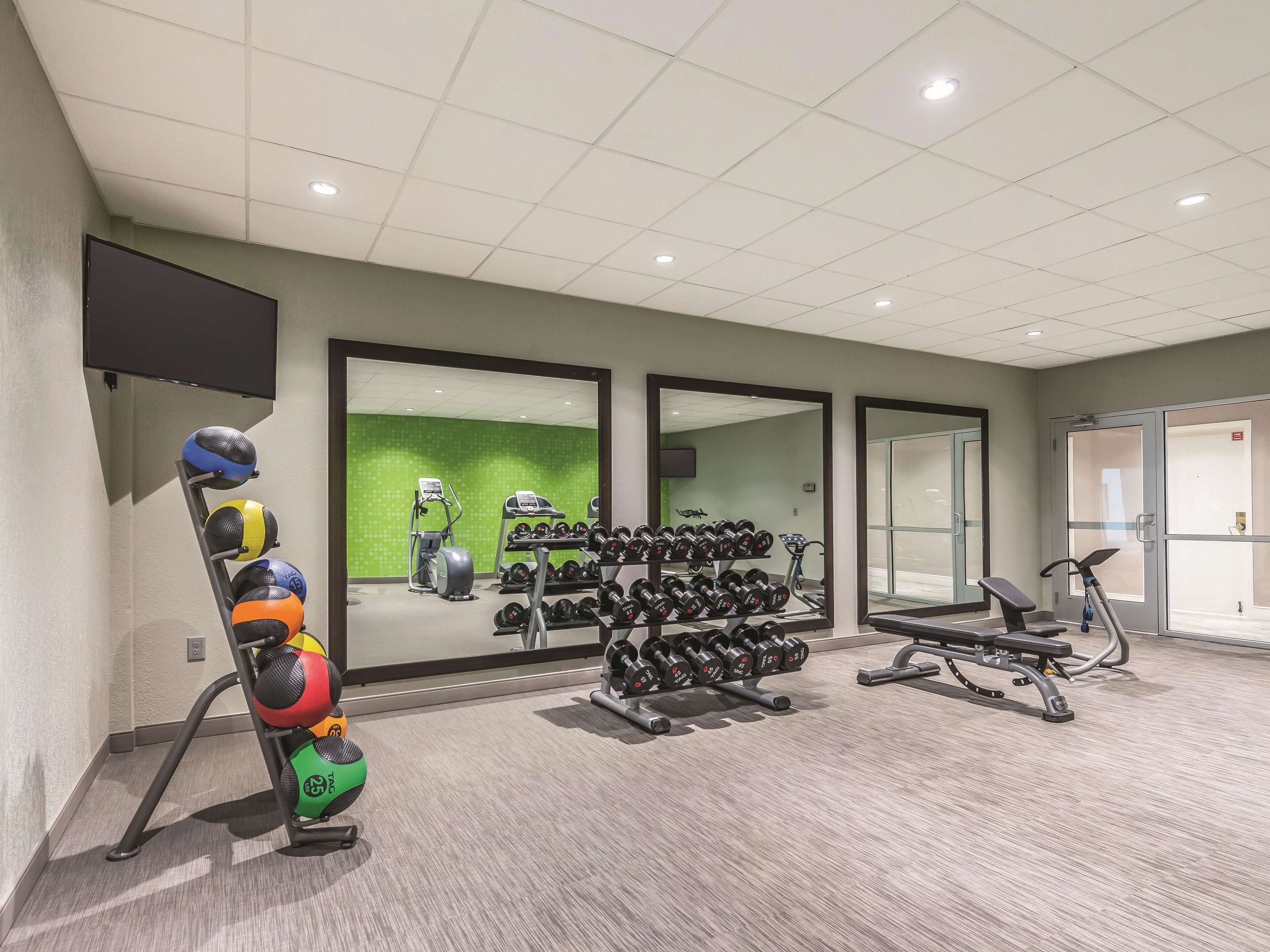 A gym with exercise equipment, a wall-mounted TV, and a green wall.