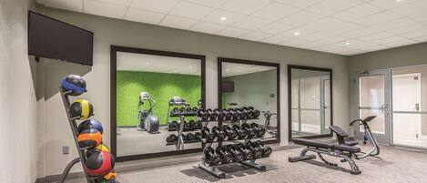 A gym with exercise equipment, a wall-mounted TV, and a green wall.