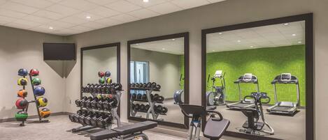 A gym with exercise equipment, mirrors, and a green wall.
