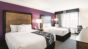 A hotel room with two beds, a desk, a chair, and a window with curtains.