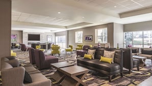 A spacious lobby with a modern design, featuring a large seating area with sofas and chairs, a reception desk, and large windows providing natural light.