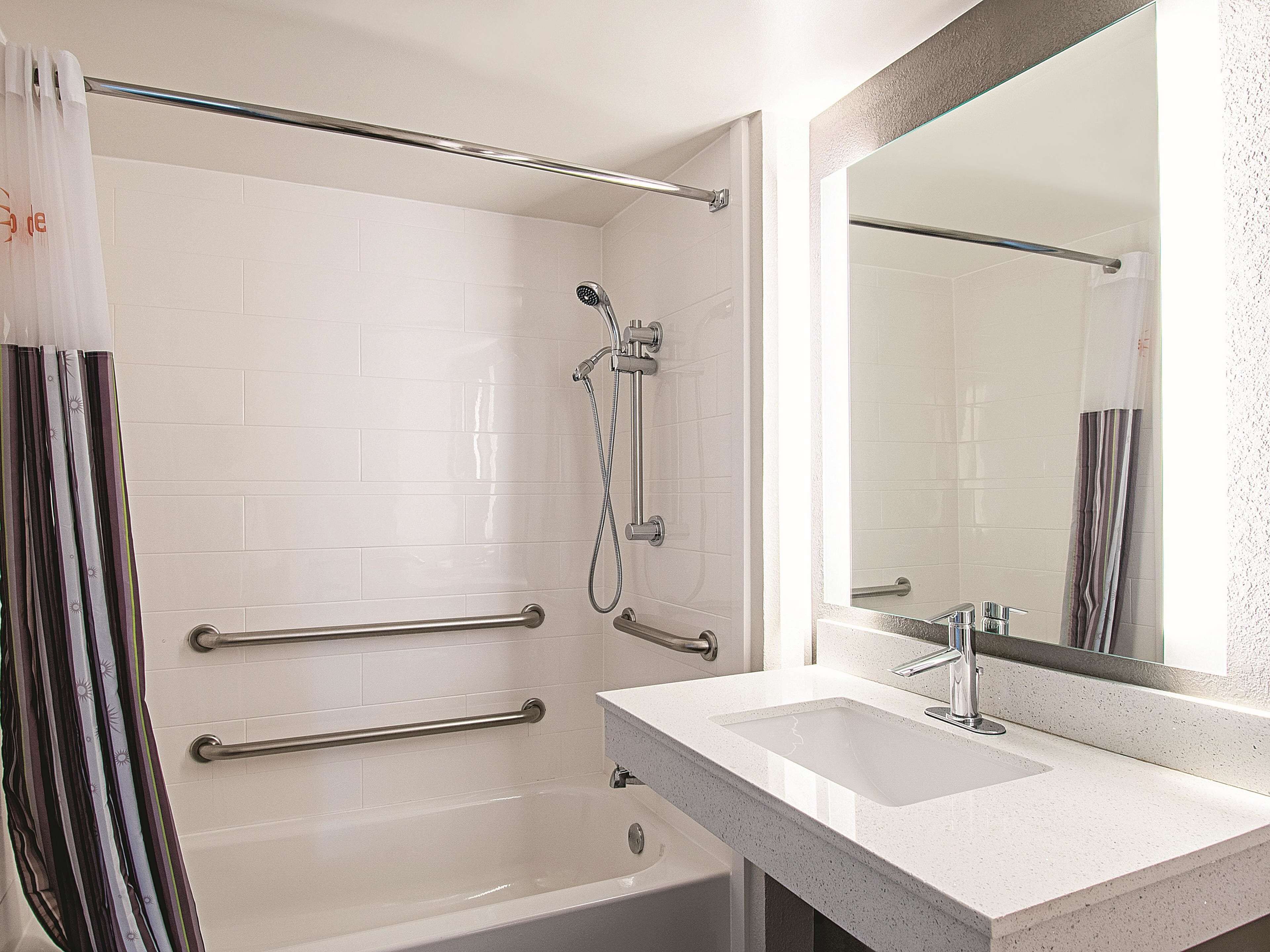 A modern bathroom with a walk-in shower, grab bars, a bathtub, and a large mirror.