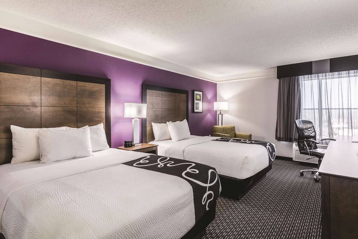 Habitación de hotel con dos camas, un escritorio, una silla y una ventana con cortinas.