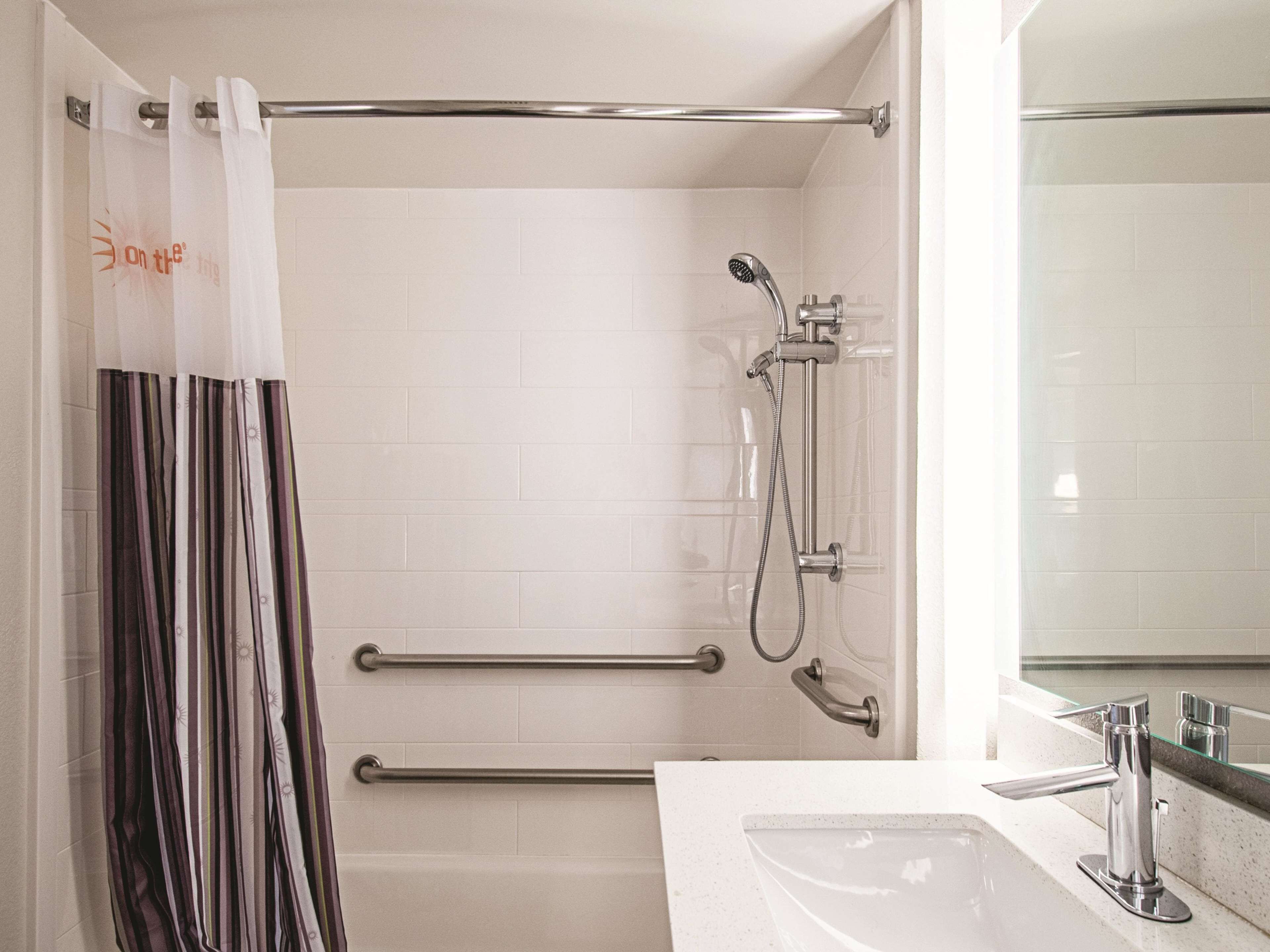 A modern bathroom with a shower, grab bars, a glass shower enclosure, and a sink with a mirror.