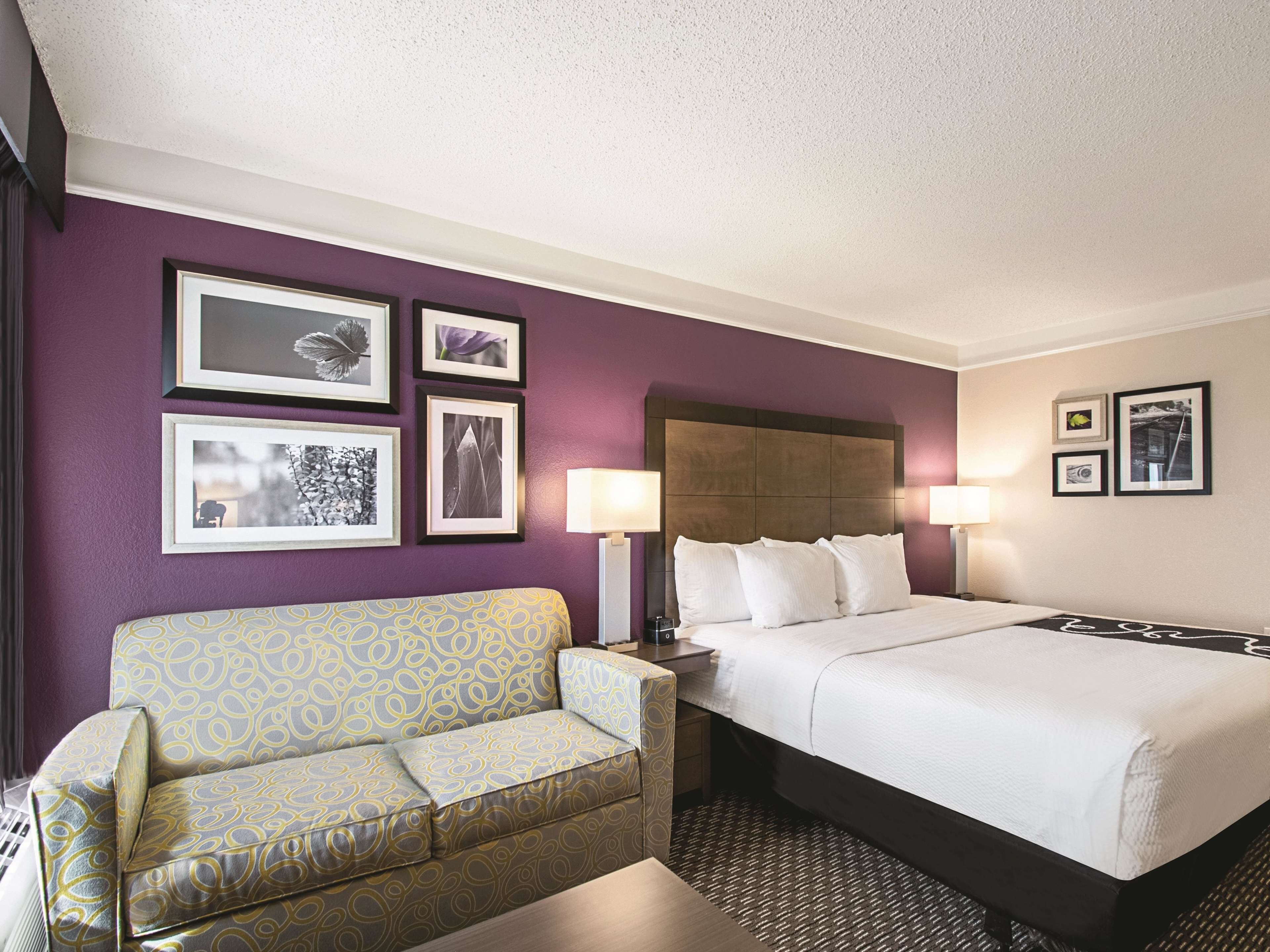A hotel room with a bed, a sofa, and wall-mounted picture frames.