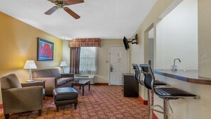 A hotel room with a ceiling fan, a sofa, a chair, a small table, a bar area with stools, and a patterned carpet. - Best Western Benton Inn (Benton)
