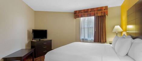Quarto de hotel com uma cama grande, televisão em uma cômoda, escrivaninha e abajur.