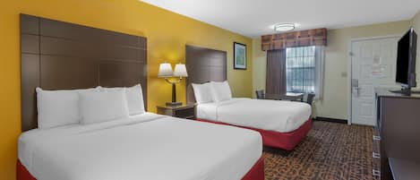 A hotel room with two beds, a desk, a television, and a window with curtains.