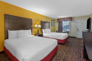 A hotel room with two beds, a desk, a television, and a window with curtains.