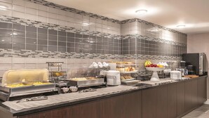 A modern kitchen with a breakfast bar, various food items, and a refrigerator. - La Quinta Inn & Suites by Wyndham Columbia / Fort Meade (Jessup)