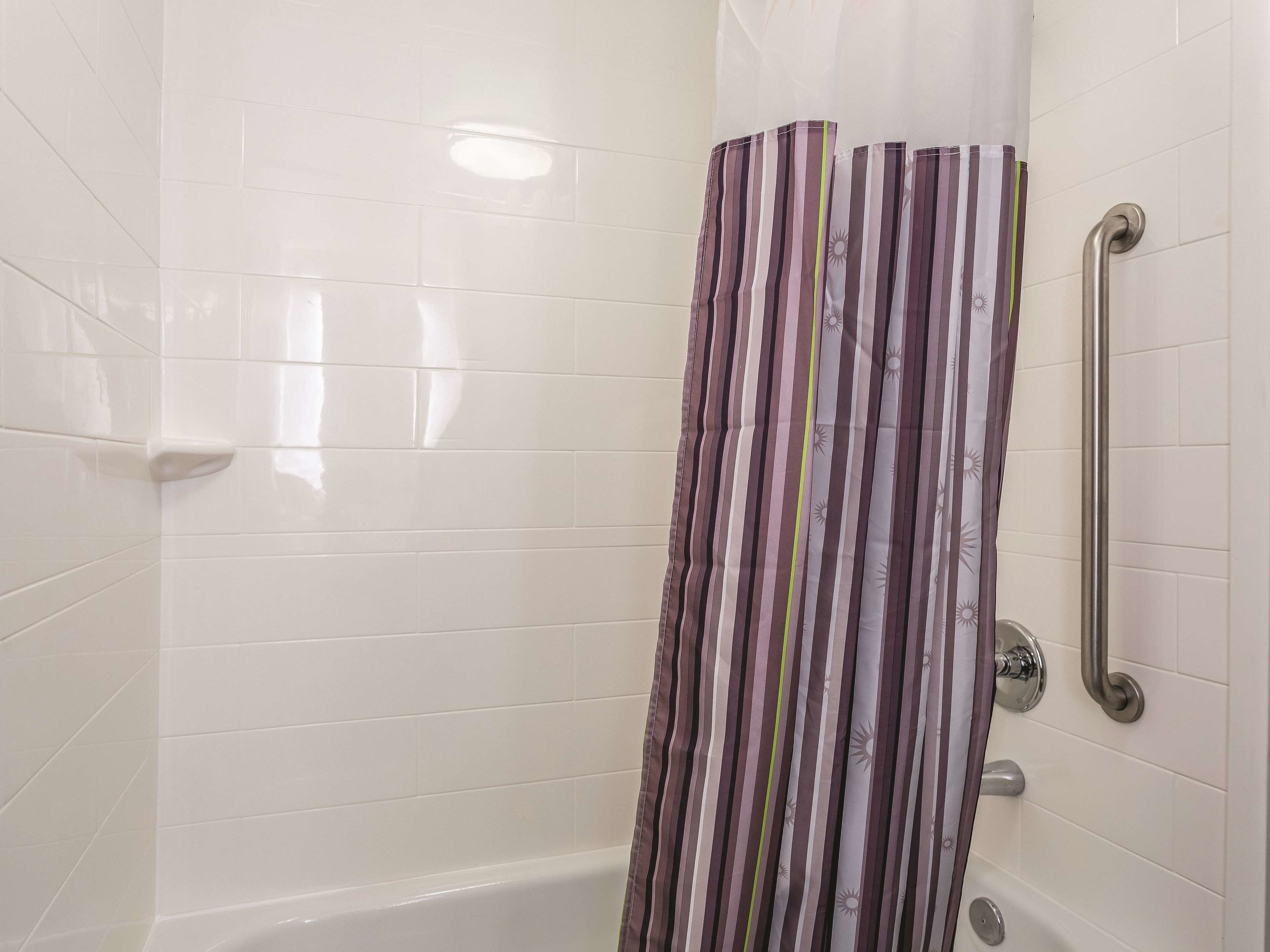 A shower area with white tiled walls, a striped shower curtain, and a grab bar on the right.