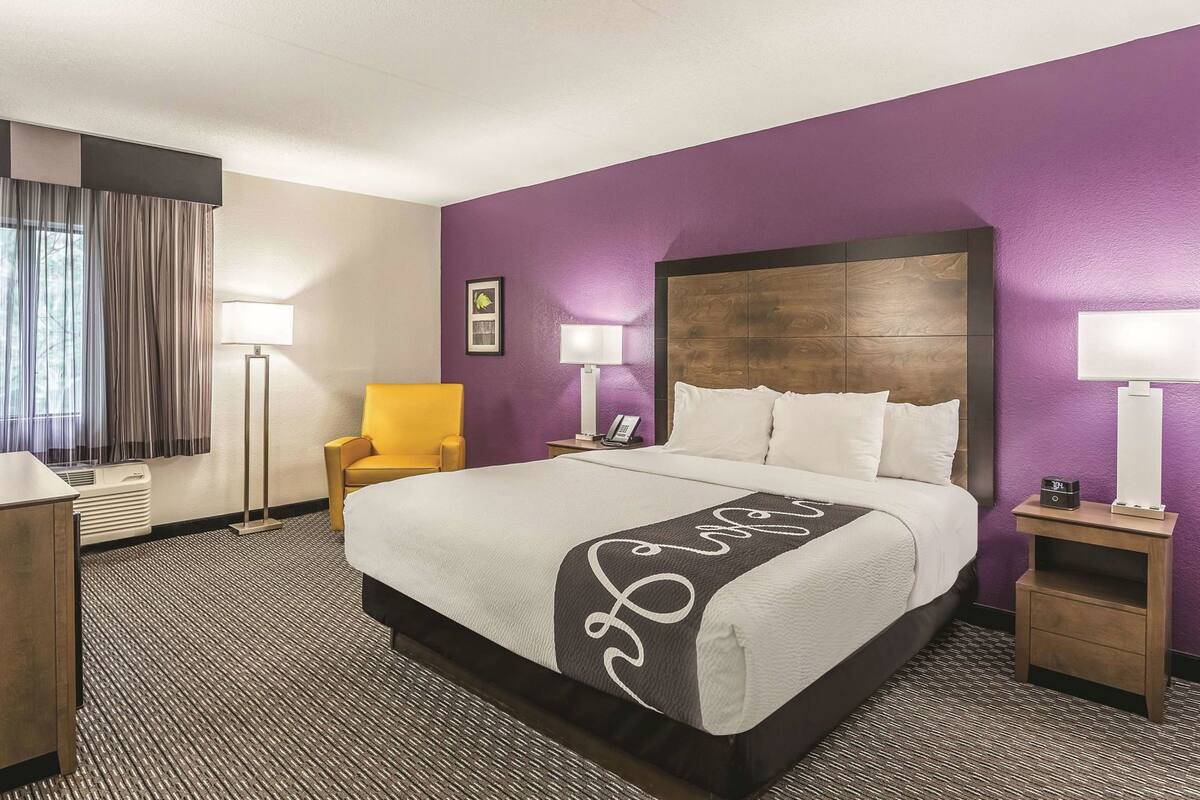 A hotel room with a large bed, a chair, a desk, and a lamp.