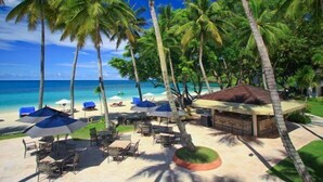 A beachside resort with palm trees, beach chairs, umbrellas, and a small hut. - Palau Pacific Resort (Meyungs)