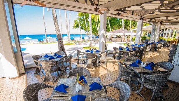 An outdoor dining area with wicker furniture and blue napkins, overlooking a beach and ocean. - Palau Pacific Resort (Meyungs)