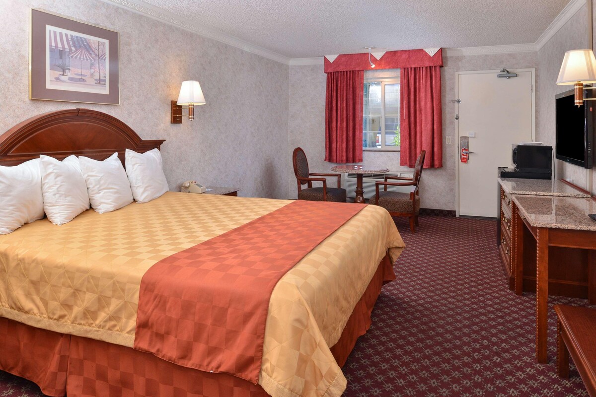 A hotel room with a large bed, a desk with a chair, a television, and a window with curtains.