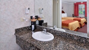 Un baño de hotel con lavamanos de encimera de granito, un espejo y dos secadores de pelo fijados a la pared.