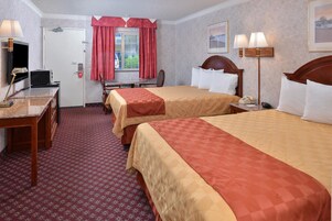 Habitación de hotel con dos camas, un escritorio con computadora, teléfono y ventana con cortinas rojas.