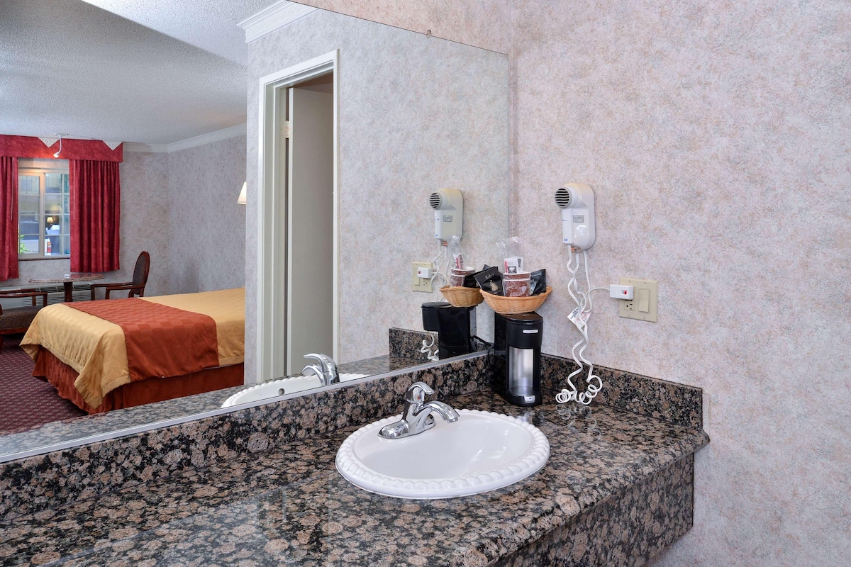 A hotel bathroom with a granite countertop, a white sink, a mirror, and a hairdryer on the wall.