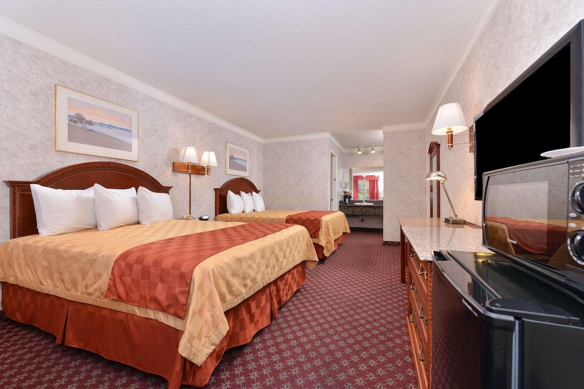 A hotel room with two beds, a TV, a desk, and a bathroom visible in the background.