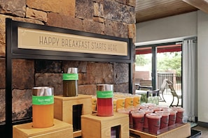 A breakfast bar with a sign that reads "HAPPY BREAKFAST STARTS HERE" and various fruit juices in dispensers.