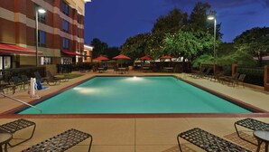 A swimming pool with lounge chairs and umbrellas, surrounded by a building with multiple floors and a fenced area with trees. - Hampton Inn Atlanta Stone Mountain (Stone Mountain)
