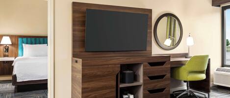 A hotel room with a bed, a desk with a chair, a flat-screen TV, a mirror, and a built-in heater.