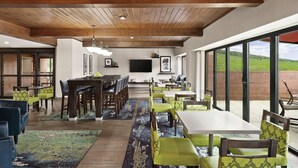 A spacious dining area with wooden tables and chairs, a flat-screen TV mounted on the wall, and large windows offering a view of the outdoors. - Hampton Inn Atlanta Stone Mountain (Stone Mountain)