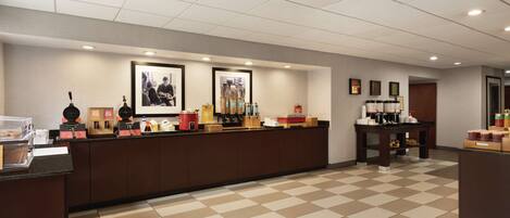 A hotel reception area with a check-in counter, framed pictures on the wall, and a coffee station.