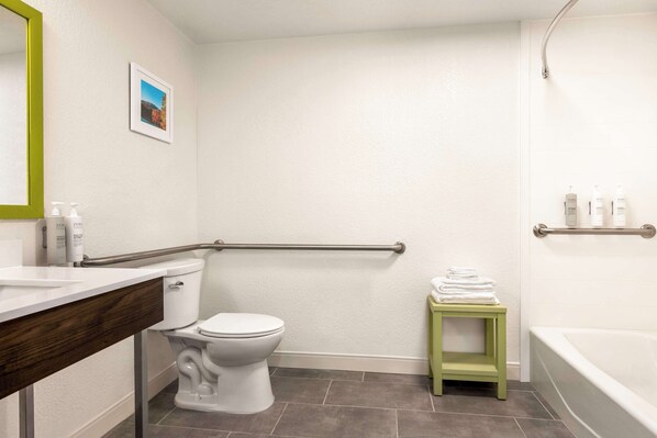 A bathroom with a white toilet, a green stool, a white sink with a wooden countertop, and a bathtub.