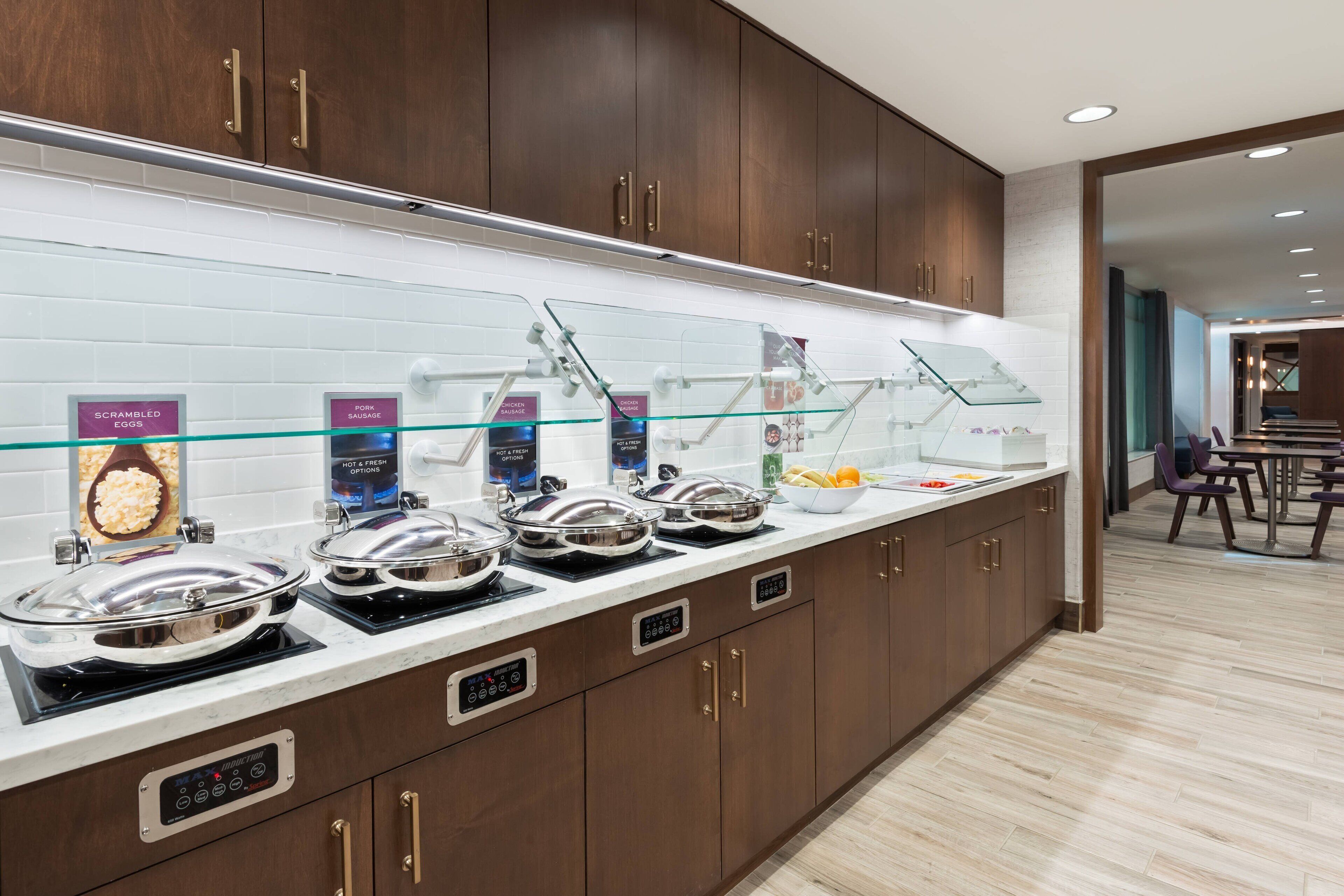 A breakfast bar with various food stations, including scrambled eggs, sausage, and chicken sausage.