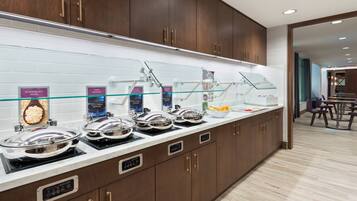 A breakfast bar with various food stations, including scrambled eggs, sausage, and chicken sausage.