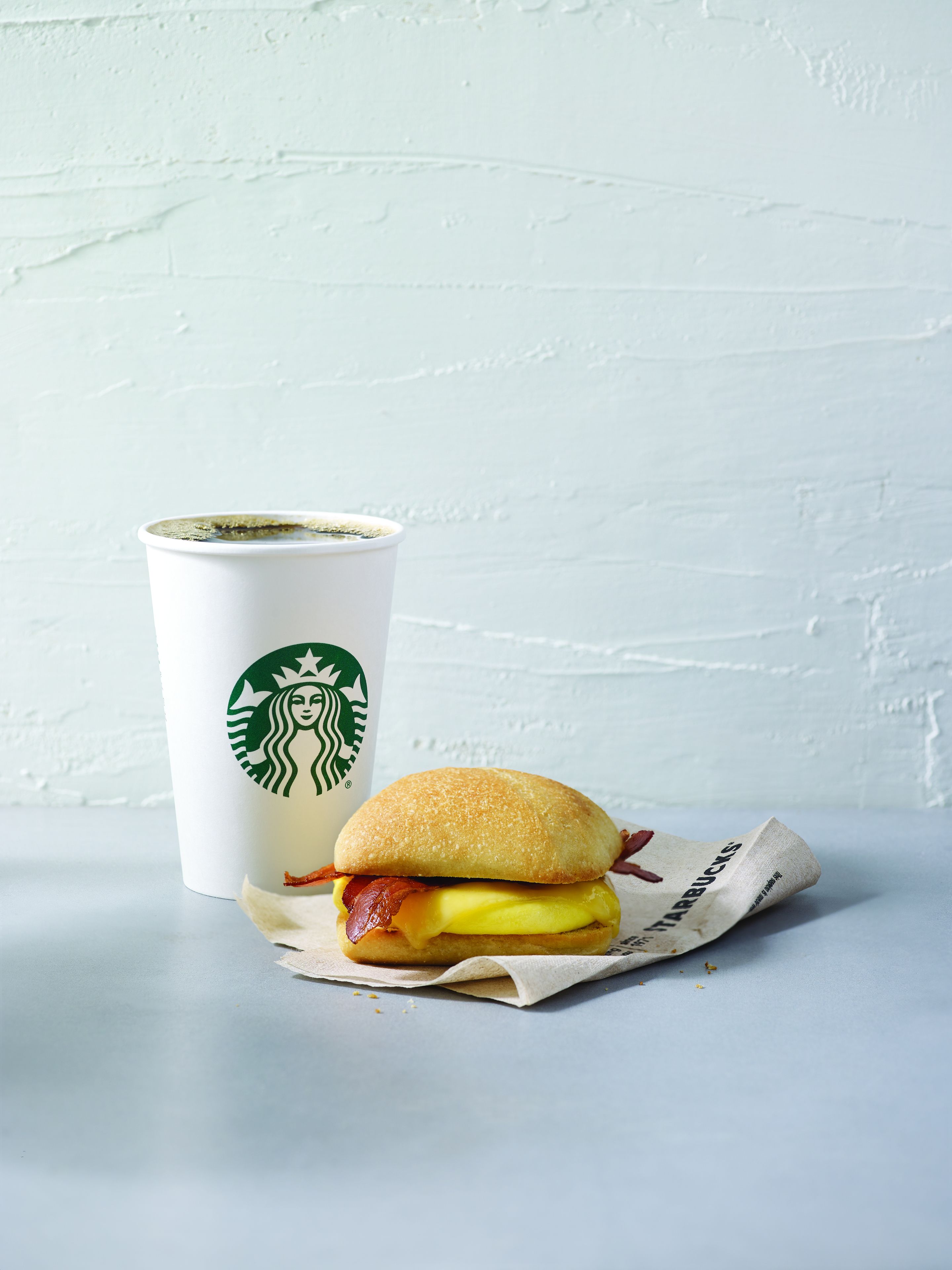 A sandwich and a Starbucks cup on a table.