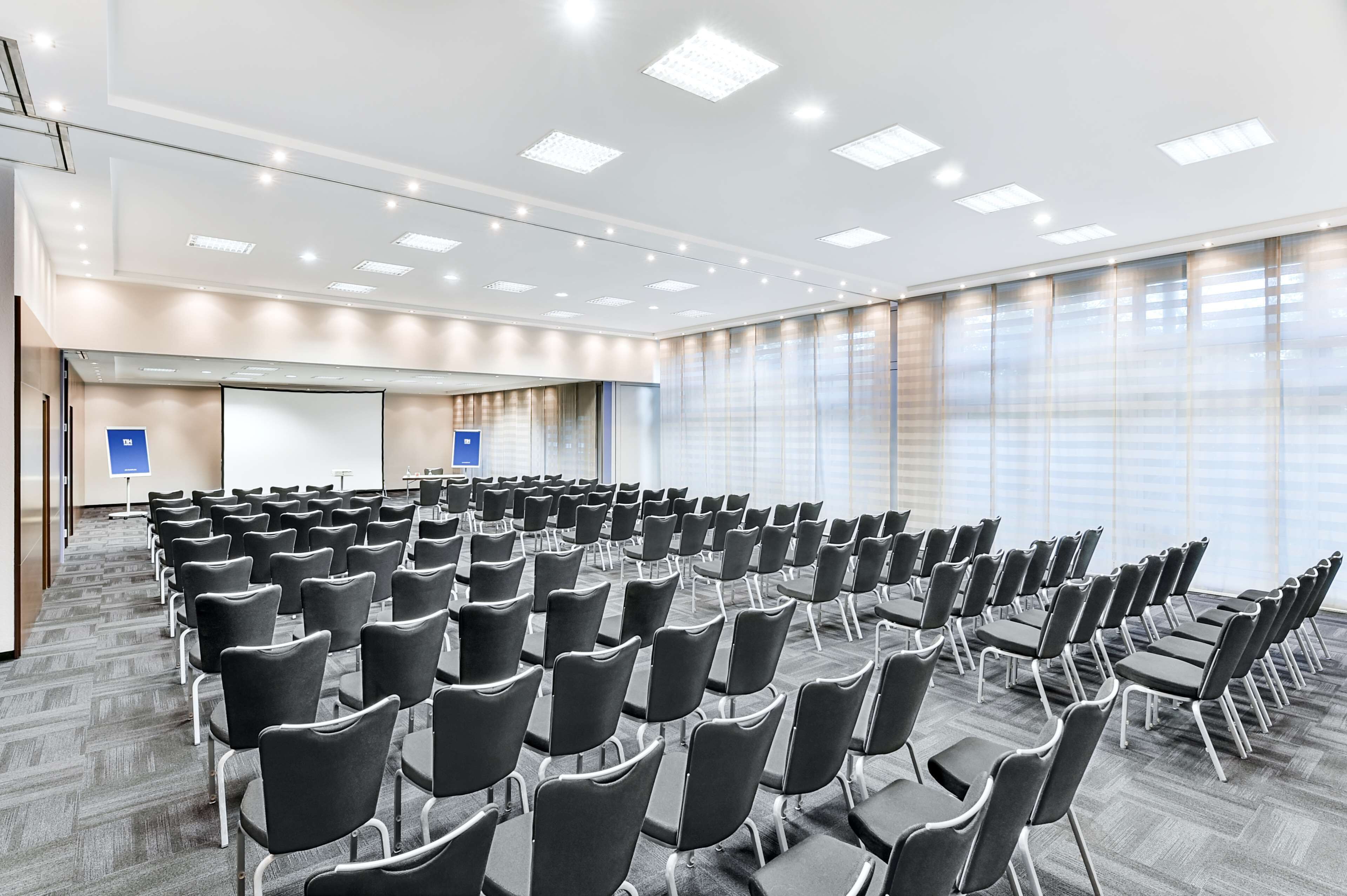 A conference room with rows of chairs, a projector screen, and large windows.