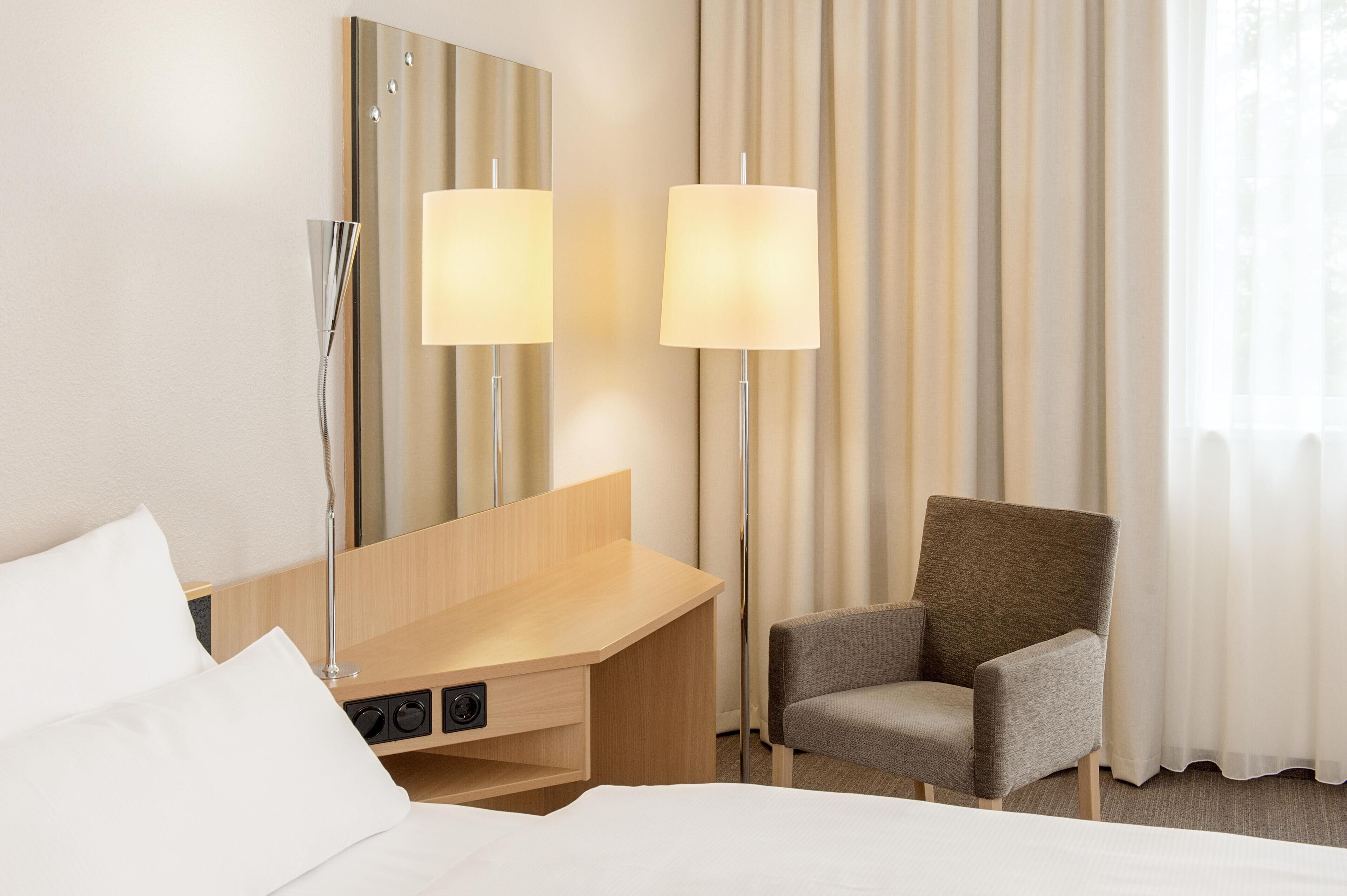 Habitación de hotel con cama, escritorio, dos lámparas, una silla y un espejo grande.