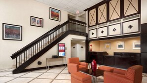 A lobby with a staircase, orange seating, a fireplace, and framed artwork on the walls. - Ramada by Wyndham Newark/Wilmington (Newark)