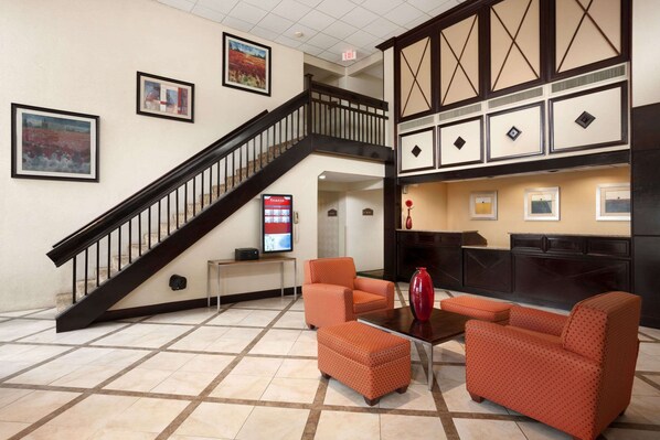 A lobby with a staircase, orange seating, a fireplace, and framed artwork on the walls.