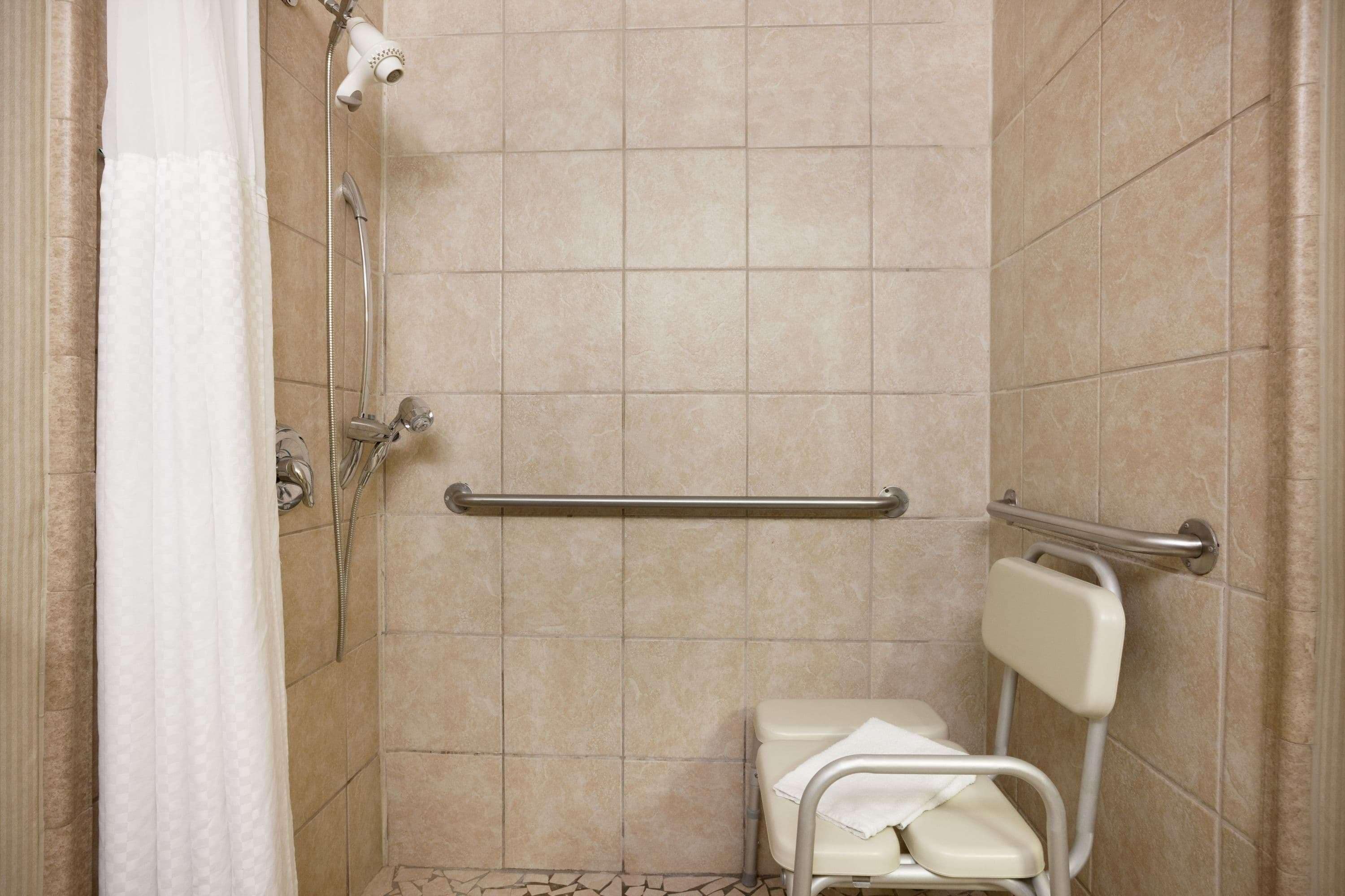 Une salle de bain équipée d’une douche, de barres d’appui, de toilettes et d’un porte-serviettes.