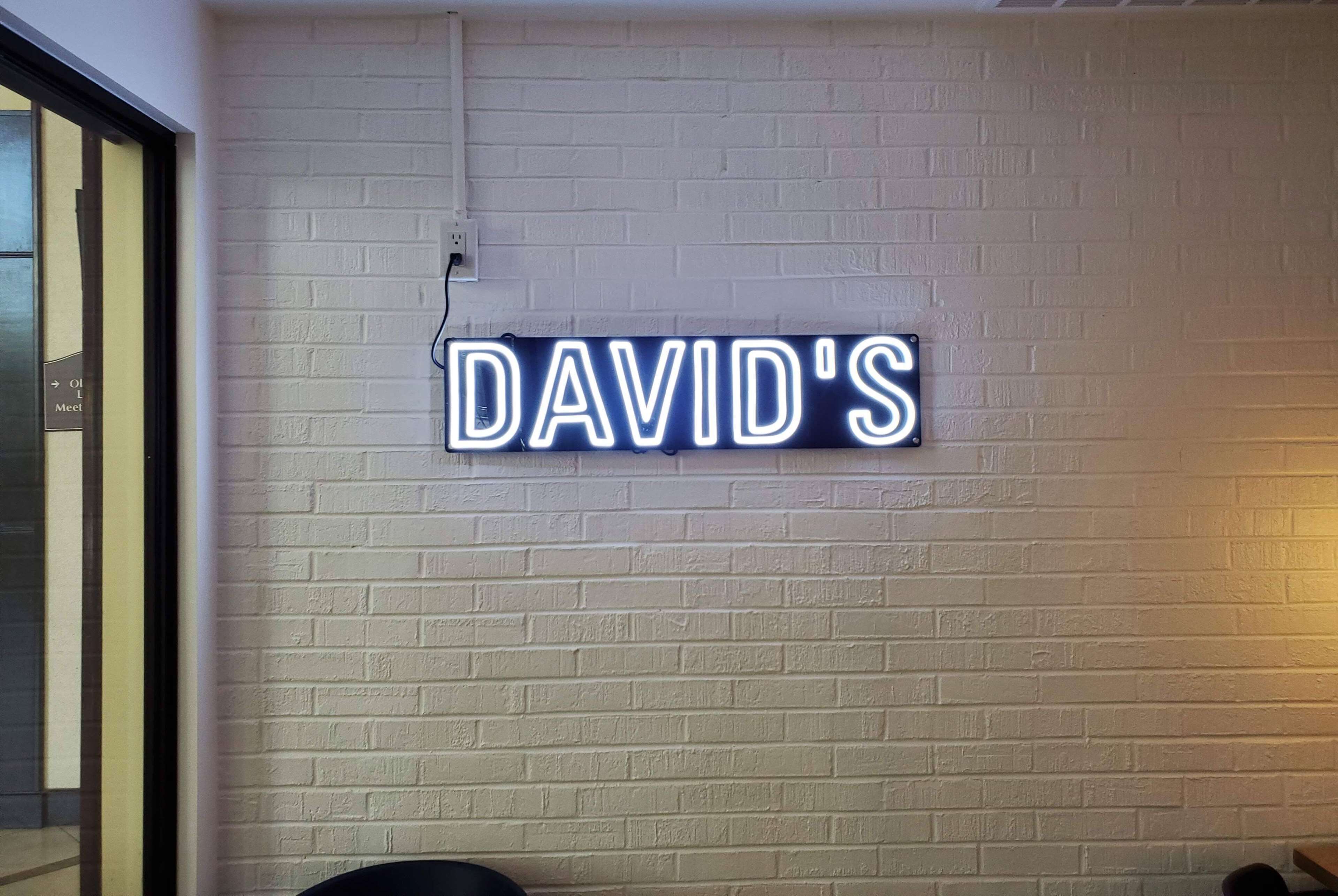 Een neonbord op een bakstenen muur met de tekst 'DAVID'S'.