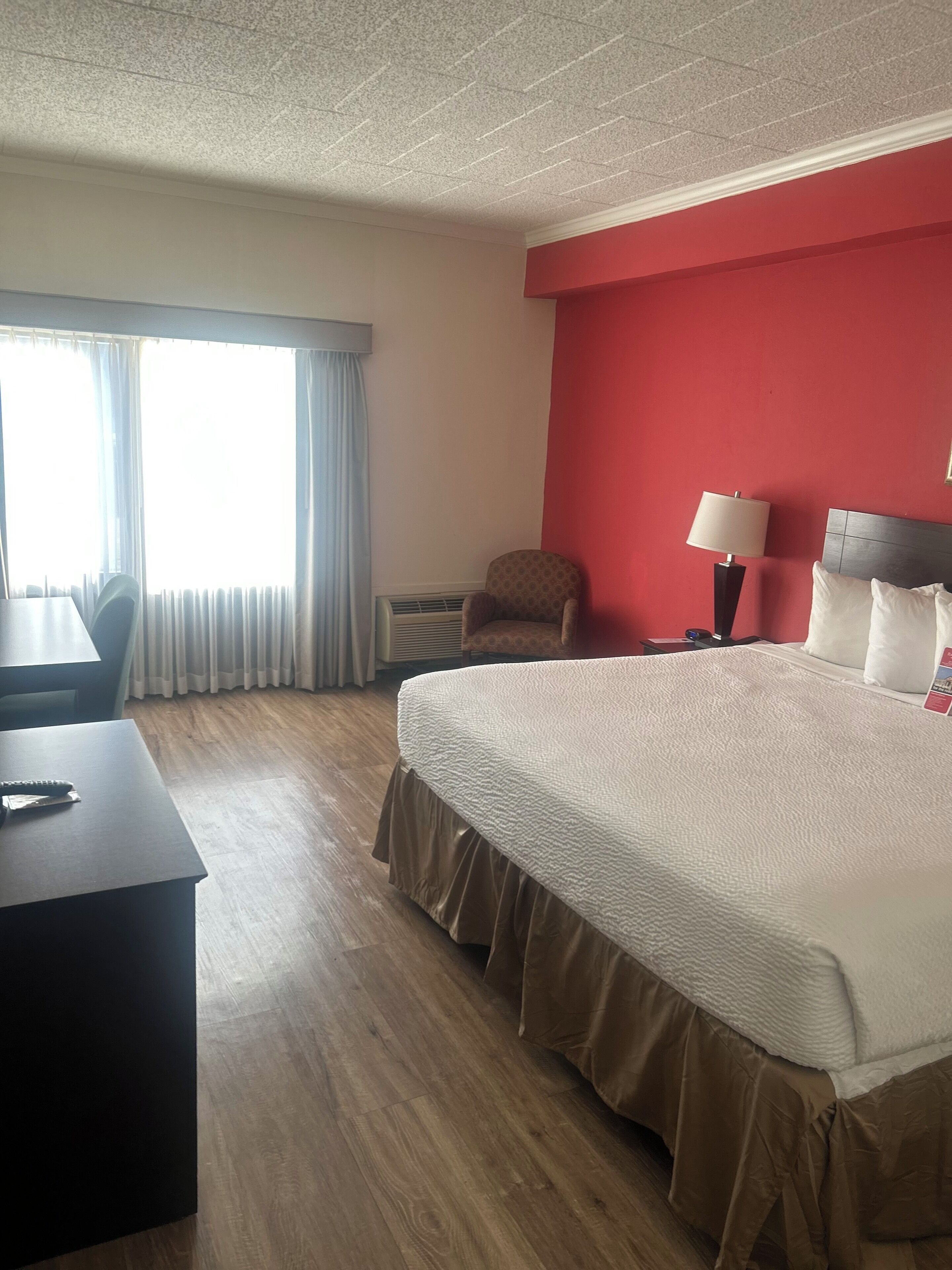 Une chambre d’hôtel avec un grand lit, un bureau, une chaise, une lampe et une fenêtre avec des rideaux.