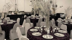 A banquet hall with round tables covered in dark tablecloths, white chairs, and floral centerpieces. - Ramada by Wyndham Newark/Wilmington (Newark)
