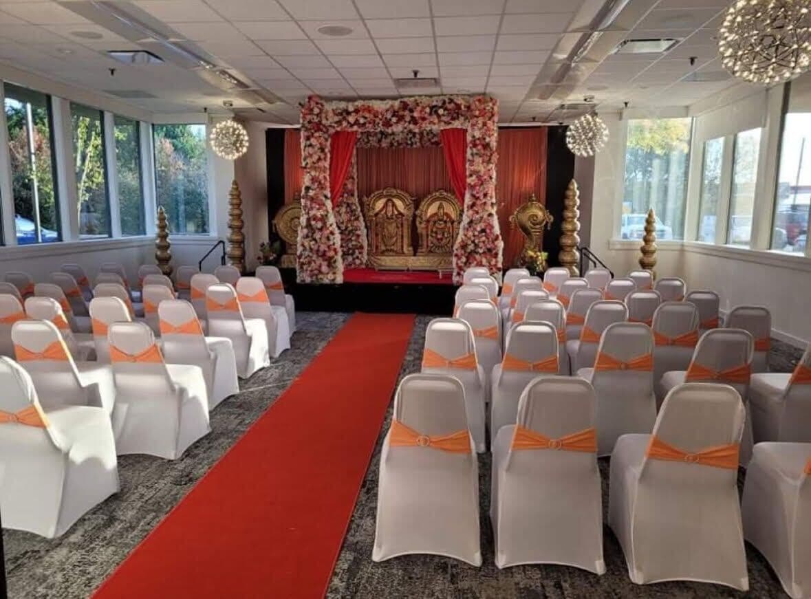 Un salón de conferencias con filas de sillas, una alfombra roja y un escenario con adornos florales.