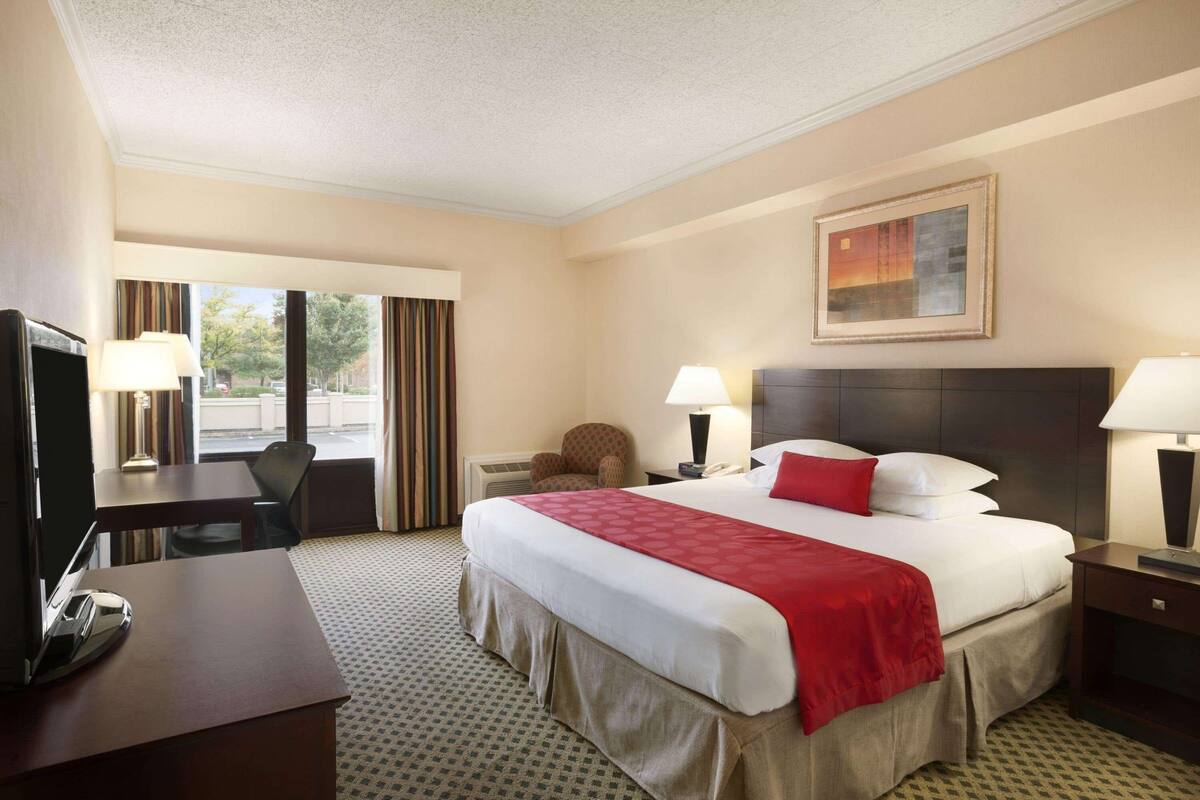 Une chambre d’hôtel avec un grand lit, un bureau, une chaise, une télévision et une fenêtre avec des rideaux.