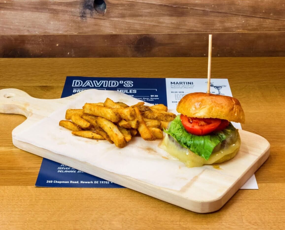 Un repas composé d’un hamburger, d’une brochette et de frites, servis sur une table en bois, avec un menu à proximité.
