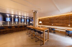 A modern bar area with a long wooden bar counter, multiple bar stools, and a seating area with tables and chairs. - Ramada by Wyndham Newark/Wilmington (Newark)